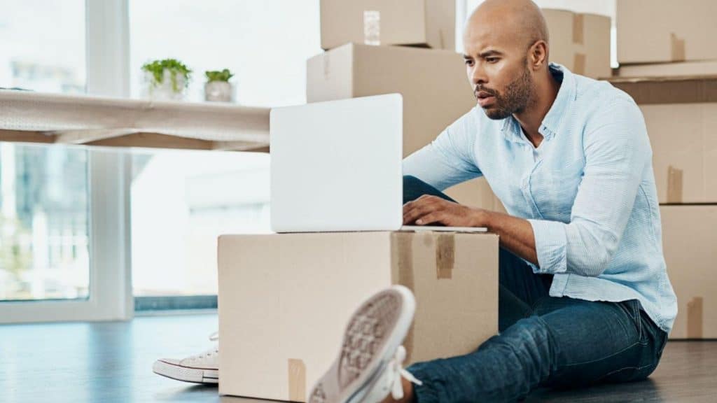 Small moving company owner researching local online marketing tips for small businesses on a laptop surrounded by moving boxes.