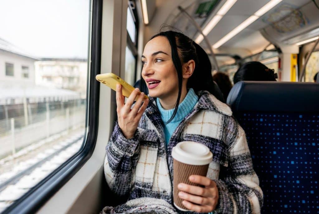 Woman commuting by train holding takeaway coffee and speaking on smartphone, enjoying a busy morning routine in Clarendon.