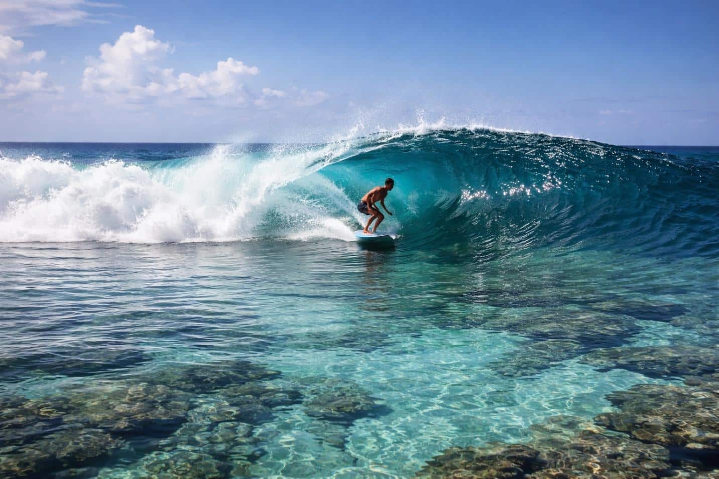 A clean peeling wave over visible reef, shot from the channel with a surfer mid-face, no crowd in frame.